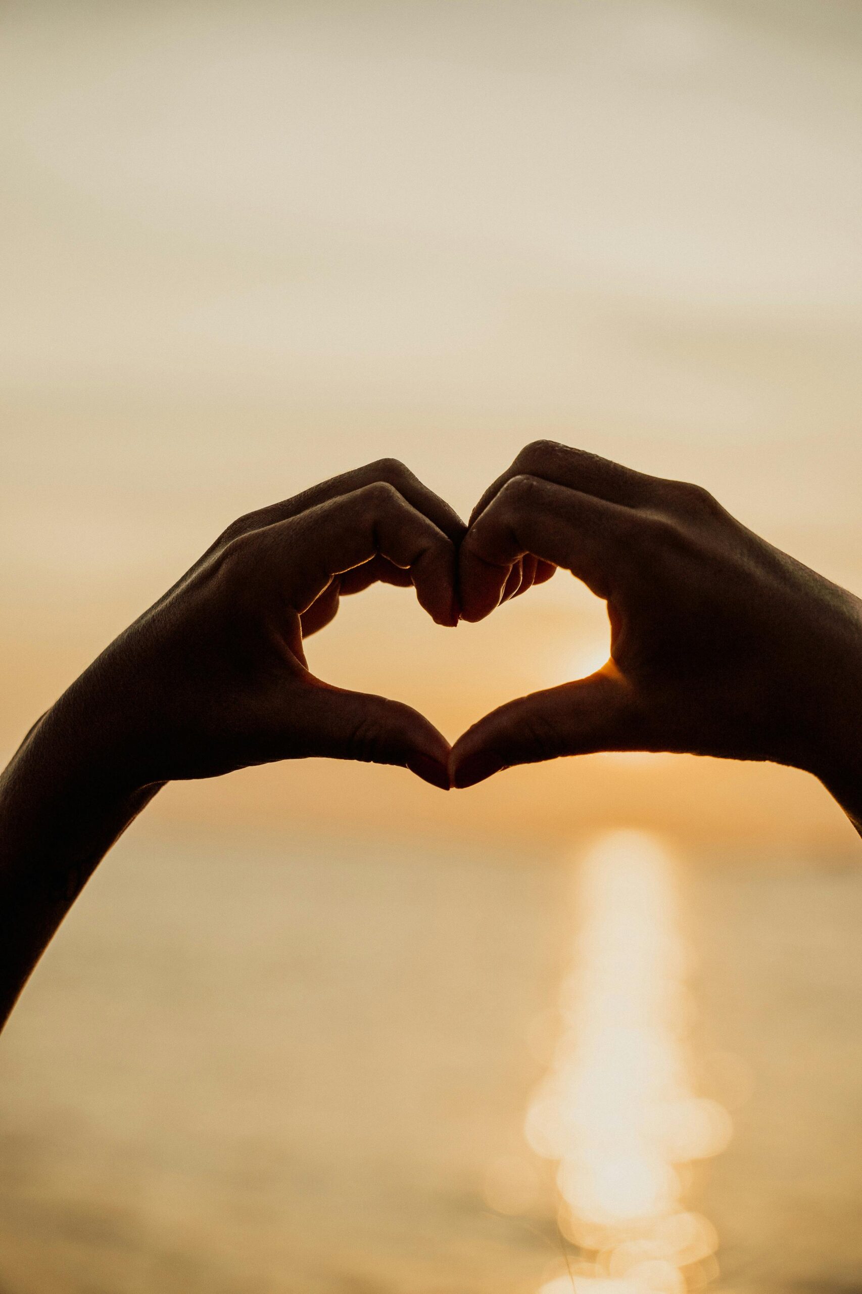 Silhouette of hands forming a heart shape against a golden sunset, conveying love and romance.
